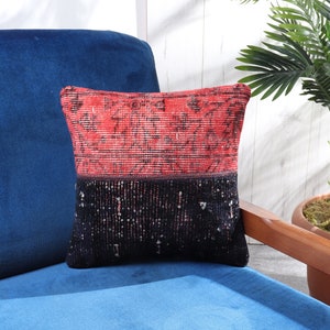 May include: A red and black patterned throw pillow with a geometric design. The pillow is sitting on a blue couch.