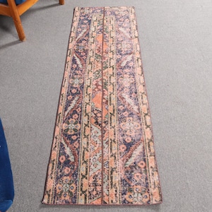 May include: A long, narrow rug with a traditional Persian design. The rug has a dark blue background with intricate patterns in shades of pink, orange, and cream.