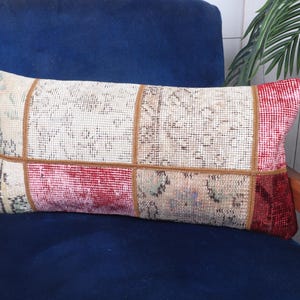 Puede incluir: Cojín decorativo rectangular con diseño patchwork. El cojín presenta una combinación de colores crema, rojo y marrón. Está colocado sobre una silla azul con brazos de madera. El diseño parece estar hecho con una alfombra vintage.