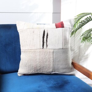 May include: A white and cream patchwork throw pillow with black and red accents. The pillow is sitting on a blue armchair.