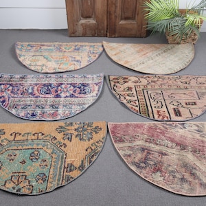 Op de afbeelding: Zes halve cirkel tapijten met ingewikkelde patronen en vervaagde kleuren. De tapijten hebben verschillende ontwerpen, waaronder bloemen- en geometrische motieven, in tinten blauw, oranje en roze. De tapijten zijn gerangschikt op een grijze ondergrond.
