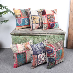 May include: Five colorful patchwork throw pillows with various patterns and colors, including red, blue, green, and yellow. The pillows are arranged on a wooden chest with a green painted surface.