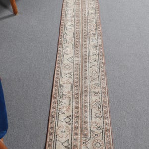 May include: A long, narrow runner rug with a beige background and intricate brown and black geometric patterns. The rug has a traditional design and would add a touch of elegance to any room.