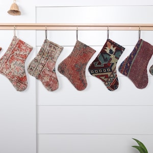 May include: Eight colorful patterned stockings hang from a wooden rod. The stockings are made from fabric with a variety of colors and designs, including red, blue, green, and brown.