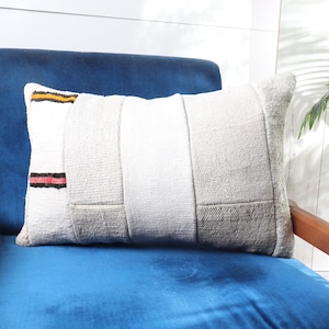 May include: A white and grey patterned throw pillow with red and yellow stripes on a blue velvet armchair.