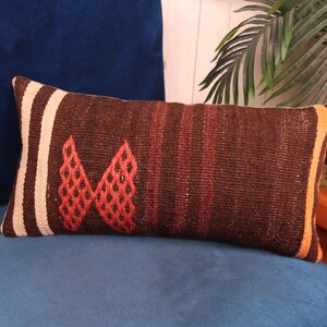 May include: A brown and red patterned throw pillow with a white border. The pillow is made of woven fabric and has a rectangular shape.