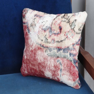 May include: A red, white, and blue patterned throw pillow with a geometric design. The pillow is sitting on a blue couch.