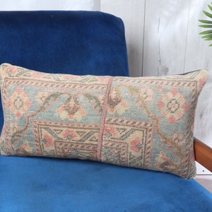 May include: A long, rectangular throw pillow with a blue, pink, and beige patterned design. The pillow is sitting on a blue velvet armchair.
