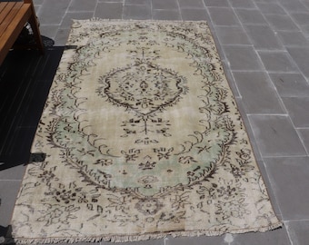 May include: A vintage rug with a cream background and a floral pattern in shades of brown and green. The rug has a fringed edge.