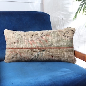 May include: A blue velvet armchair with a decorative throw pillow featuring a woven pattern in shades of beige, brown, and red. The pillow has a brown leather trim.