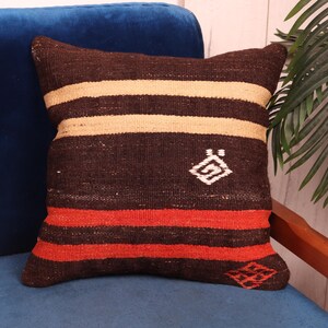 May include: A brown, beige, and red striped throw pillow with a geometric design in the center. The pillow is on a blue velvet couch.