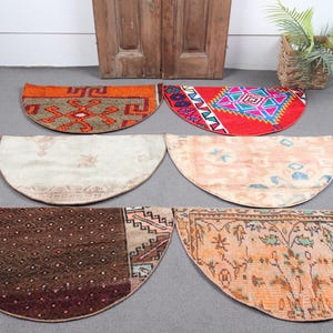 Puede incluir: Seis alfombras semicirculares con patrones intrincados y colores variados se muestran sobre una superficie gris. Las alfombras presentan diseños en tonos naranja, rojo, marrón y crema. Las alfombras probablemente están hechas de materiales tejidos.