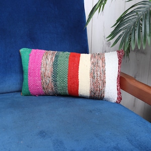 May include: A colorful striped throw pillow with red, pink, green, and white stripes. The pillow is made of woven fabric and has a slightly textured surface.