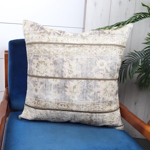 Puede incluir: Un cojín de tiro blanco y gris con un patrón y un borde marrón se sienta en una silla de terciopelo azul con brazos de madera.