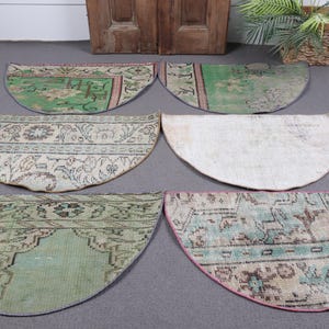 Puede incluir: Se muestran seis alfombras semicirculares con colores descoloridos y patrones intrincados. Las alfombras presentan tonos de verde, beige y azul, con un borde rosa en una de ellas. Las alfombras están dispuestas sobre una superficie gris.