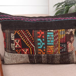 May include: Rectangular cushion with a dark brown top and a patchwork design. The patchwork features geometric patterns in red, orange, and turquoise. The cushion is resting on a beige chair.