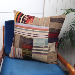 May include: A colorful patchwork pillow with a variety of textures and patterns. The pillow is made of woven fabric and has a rectangular shape. It is sitting on a blue velvet chair with wooden arms.