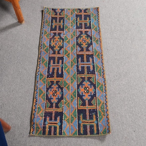 May include: A blue, green, orange, and white patterned rug with geometric designs. The rug has a long, narrow shape.