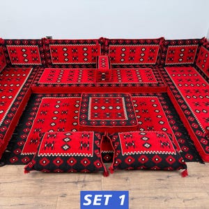 May include: A modular floor seating set featuring a vibrant red and black geometric pattern. The set includes long floor cushions, backrest cushions, a central square ottoman, and two floor pillows, all decorated with intricate white and black motifs.