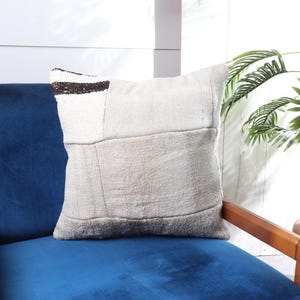 May include: A white and brown patchwork throw pillow with a blue velvet armchair in the background.