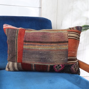 May include: A colorful, striped throw pillow with a patchwork design. The pillow is made of woven fabric and has a variety of colors, including red, brown, beige, and blue. The pillow is sitting on a blue velvet chair.
