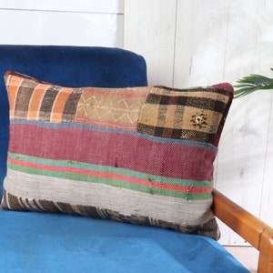 May include: A colorful patchwork pillow with a variety of textures and patterns, including stripes, plaid, and geometric designs. The pillow is resting on a blue velvet armchair.