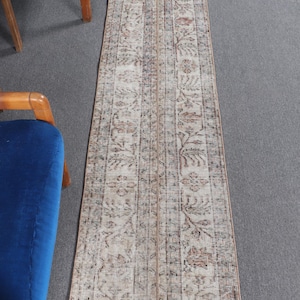 May include: A long, rectangular rug with a beige background and a brown floral pattern. The rug has a distressed look and is perfect for adding a touch of vintage style to any room.