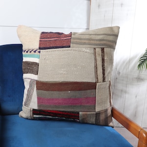 May include: A patchwork pillow with a variety of colors and textures, including brown, beige, pink, and blue. The pillow is sitting on a blue velvet chair.