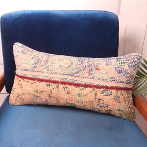 May include: A decorative throw pillow with a beige background and a blue, red, and green geometric pattern. The pillow is sitting on a blue velvet chair.