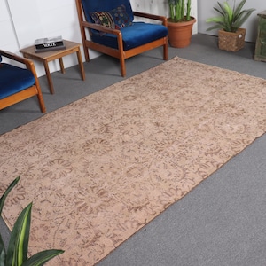 May include: A light brown patterned rug with a floral design. The rug is laid out on a gray floor with two blue chairs and a small wooden table.