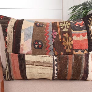May include: A rectangular patchwork cushion with a variety of colours and patterns. The cushion features a mix of brown, beige, red, and blue hues, with geometric and floral designs. It is placed on a neutral-toned chair, suggesting a rustic or bohemian style.