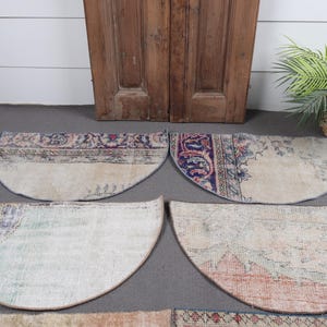 May include: Four half-circle vintage rugs with faded colors and intricate patterns. The rugs feature a mix of beige, blue, and red hues, with a distressed, antique appearance. The rugs are arranged on a gray surface.