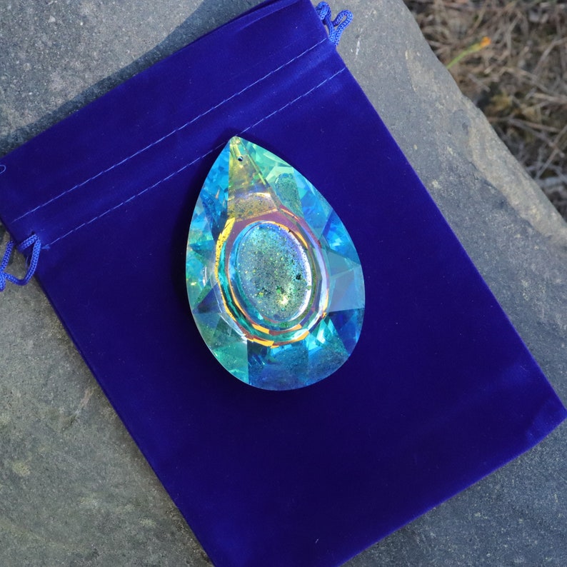 May include: A teardrop-shaped crystal prism with a rainbow iridescent finish. The prism is displayed on a blue velvet pouch.