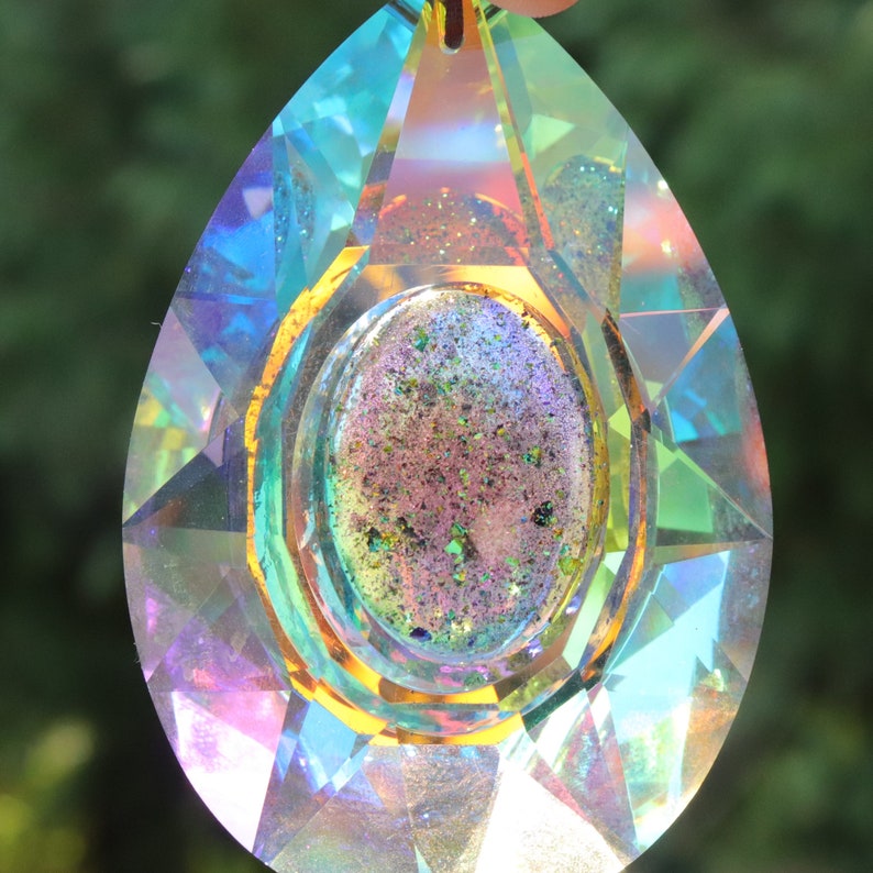 May include: A teardrop-shaped crystal prism with a gold-toned frame and a multi-colored iridescent center. The prism is made of clear glass and has a faceted design.