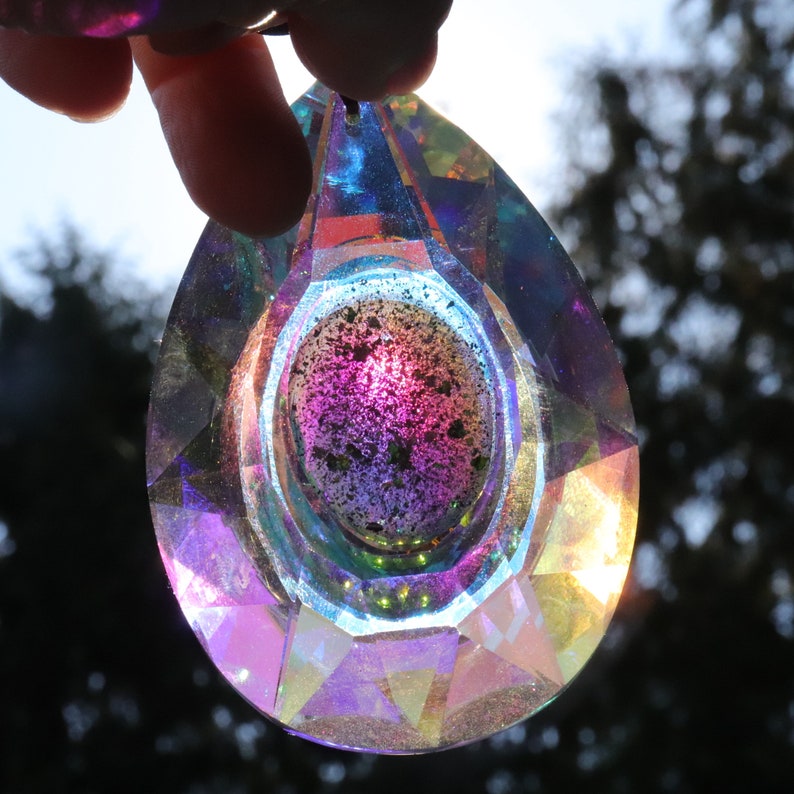 May include: A teardrop-shaped crystal prism with iridescent rainbow colors and a faceted design. The prism has a smaller, round, faceted crystal inside.