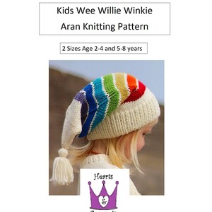 May include: A white aran knit hat with a rainbow coloured brim and a white tassel. The hat is being worn by a child. The text "Kids Wee Willie Winkie Aran Knitting Pattern" and "2 Sizes Age 2-4 and 5-8 years" is visible above the hat. The text "Hearts & Coronets" is visible below the hat.