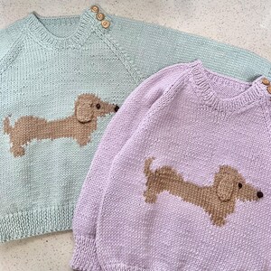 May include: Two knitted sweaters with dachshund designs. One sweater is light green with a brown dachshund, the other is light purple with a brown dachshund.