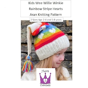 Puede incluir: Un gorro de punto de rayas arcoíris con un pompón blanco en el extremo de la cola larga. El gorro tiene un fondo blanco con una raya arcoíris y corazones blancos. El gorro es para niños y está disponible en dos tallas: 2-4 años y 5-8 años. El patrón se llama "Kids Wee Willie Winkie Rainbow Stripe Hearts Aran Knitting Pattern".