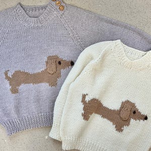 May include: Two knitted sweaters with dachshund designs. One sweater is light gray with a brown dachshund, the other is cream with a brown dachshund.