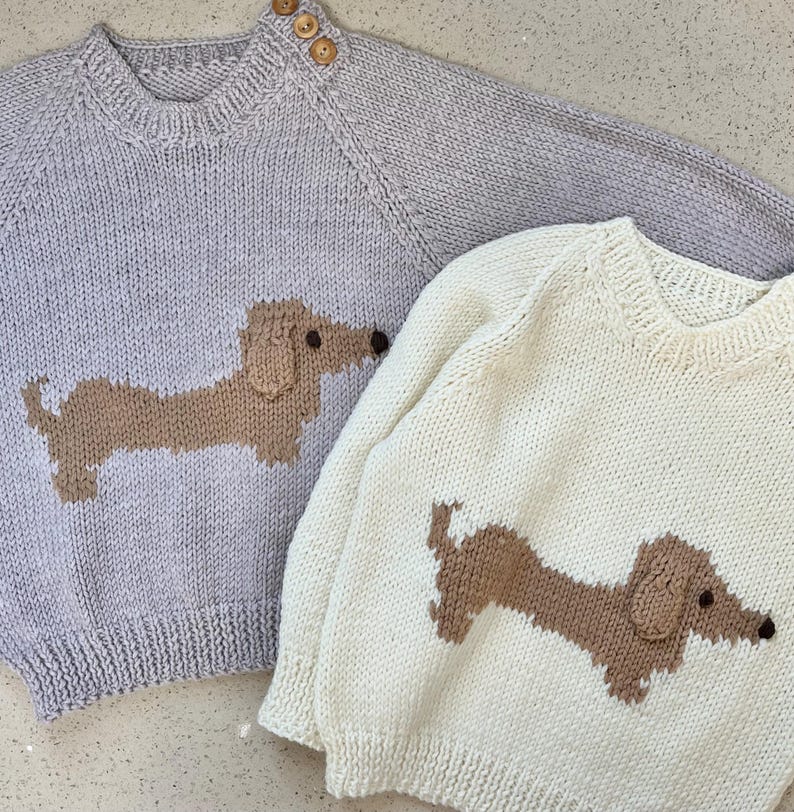 May include: Two knitted sweaters with dachshund designs. One sweater is light gray with a brown dachshund, the other is cream with a brown dachshund.