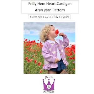 Op de afbeelding: Een kind draagt een lila vest met een geschulpte zoom en hartjes, witte hartaccenten en houten knopen. Het Aran-garenpatroon is beschikbaar voor kinderen van 1-5 jaar. De tekst "Frilly Hem Heart Cardigan" is inbegrepen.