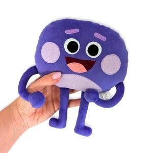 May include: Purple plush toy with a smiling face, two large purple eyes, and two small pink circles on its cheeks. The toy has long purple arms and legs.
