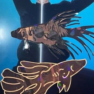 May include: Two iridescent fish-shaped stickers with a holographic effect. The stickers have a detailed design with multiple colors and are set against a blue background. The stickers appear to be decorative.