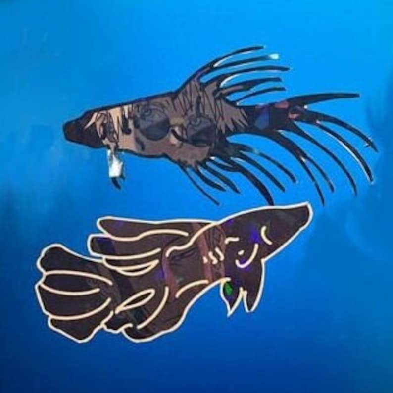 May include: Two decorative fish cutouts. The top fish is dark with spiky fins and a textured pattern. The bottom fish is a similar design, with a curved body and a smiling face. Both are set against a bright blue background.