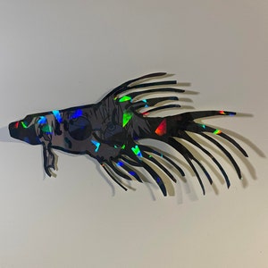 May include: A black, stylized fish-shaped art piece with iridescent, colorful accents. The artwork features a detailed illustration of a face with glasses and a complex fin design. The piece is likely a decorative item or wall art.