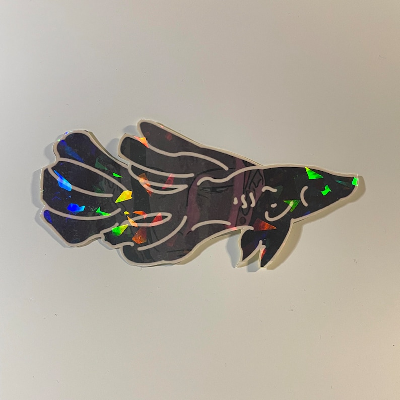 May include: A black sticker in the shape of a fish with a white outline. The fish has a smiling face and iridescent accents that reflect multiple colors. The sticker is on a white background.