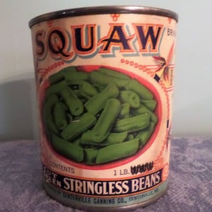 Op de afbeelding: Vintage blik van het merk SQUAW met sperziebonen zonder draad. Het etiket toont een kom met sperziebonen en de tekst "SQUAW", "STRINGLESS BEANS" en "1 LB."