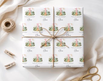 May include: White wrapping paper featuring a repeating pattern of a pink number one, green dinosaurs, and the text Happy 1st Birthday to a special little girl and the name Olivia. The paper is tied with brown twine in a bow.