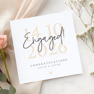 Puede incluir: Una tarjeta de compromiso blanca con la palabra "Engaged!" en escritura negra. La fecha "14 10 26" est&aacute; impresa en color beige claro. La tarjeta tambi&eacute;n incluye el texto "Congratulations David & Louise" y un peque&ntilde;o coraz&oacute;n.