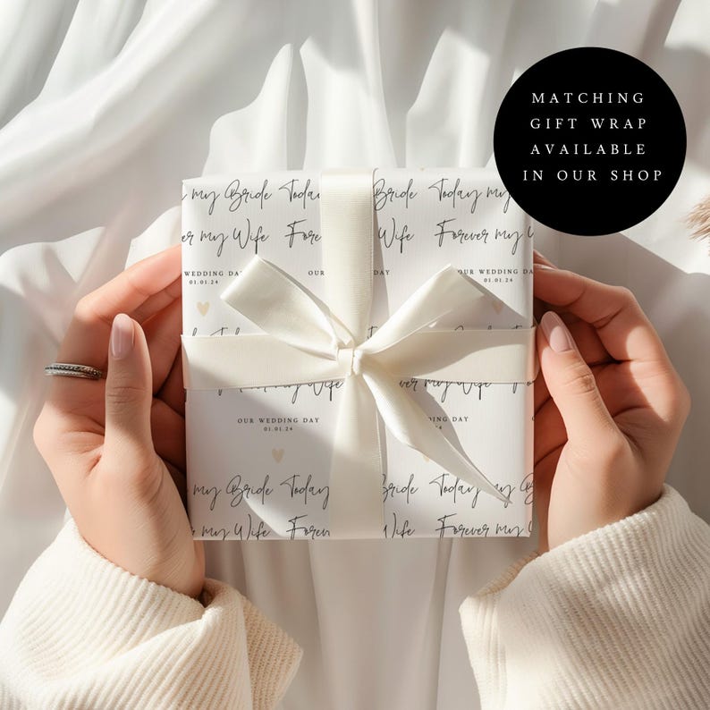 May include: A wrapped gift with a white ribbon and bow. The wrapping paper has a repeating pattern of text that reads "my Bride Today or my Wife Forever" and "Our Wedding Day". The gift is held by a person.